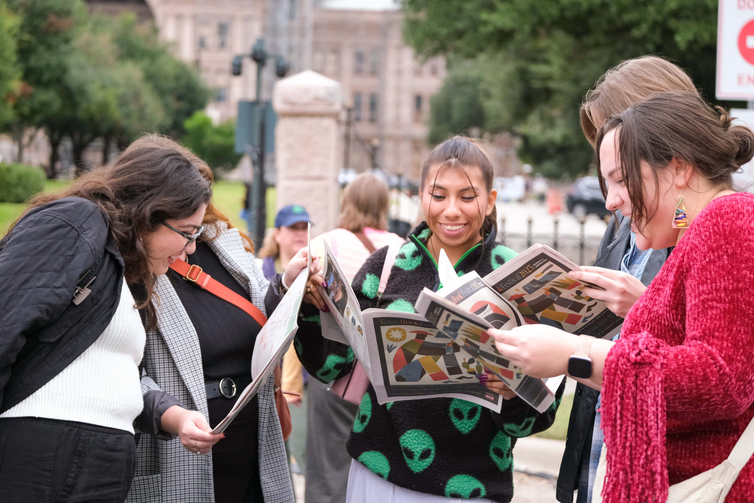 A group smiles and opens copies of the special edition of the Austin Chronicle featuring the Texas Book Festival 2023 schedule and information for festival weekend.